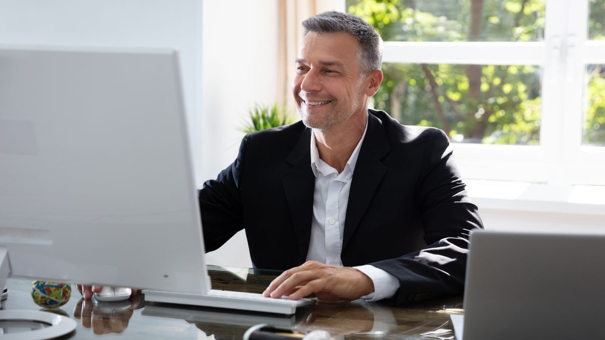 Older man in blazer sits in front of his computer trying to find the right contact person.