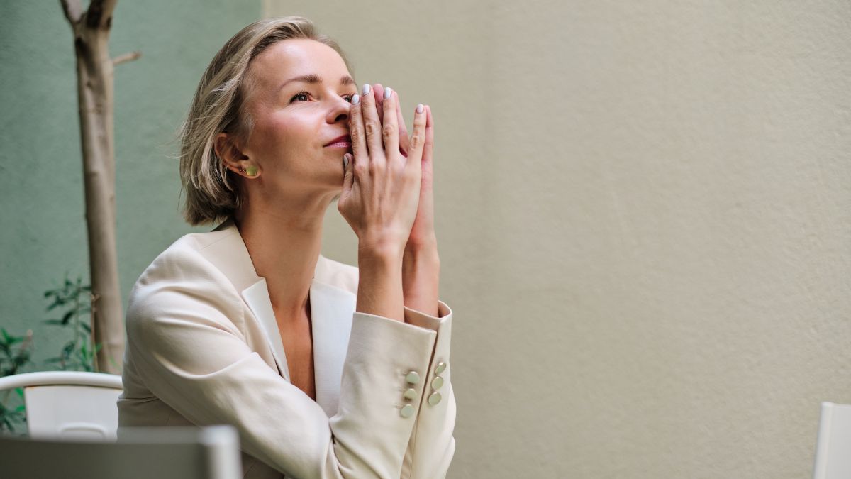 Woman sitting at table presses hands together while pondering the best opening line for her email.
