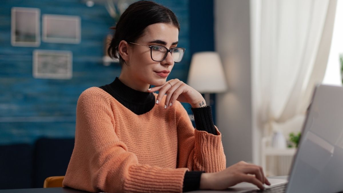 Bespectacled young woman with a hand tattoo sits before her laptop looking at an AI-managed inbox.