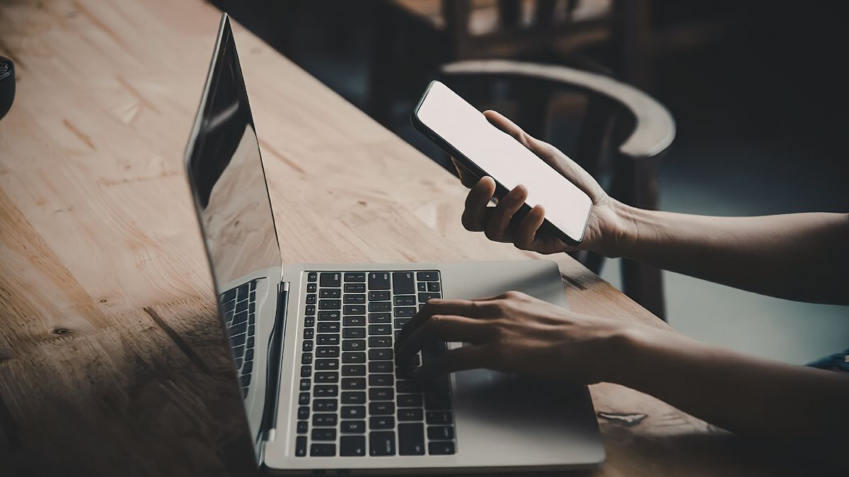 Marketer taps away at laptop while managing the smartphone to ensure great marketing.