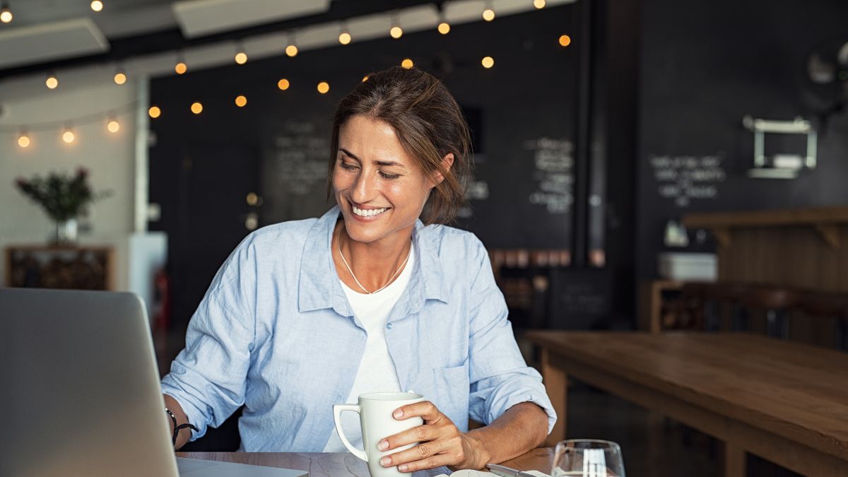 Hispanic woman clutches coffee cup and looks at laptop where she is performing an email health check.
