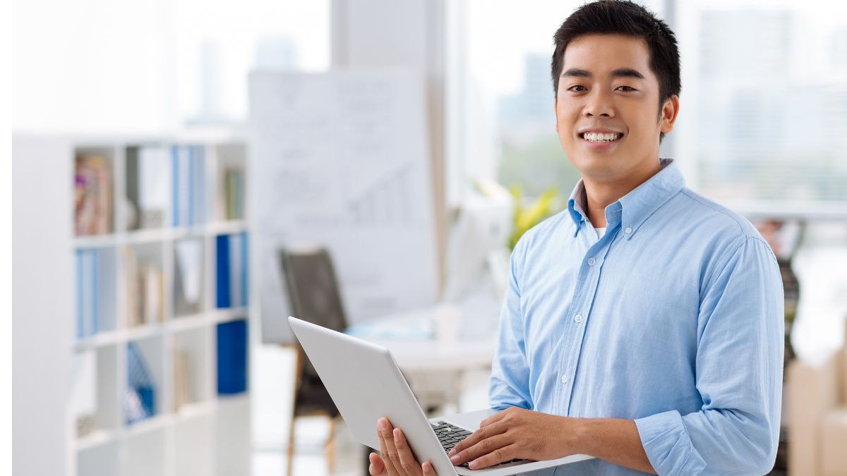 Young Asian man smiles while holding his laptop. He smiles because he knows his emails don't look like spam.